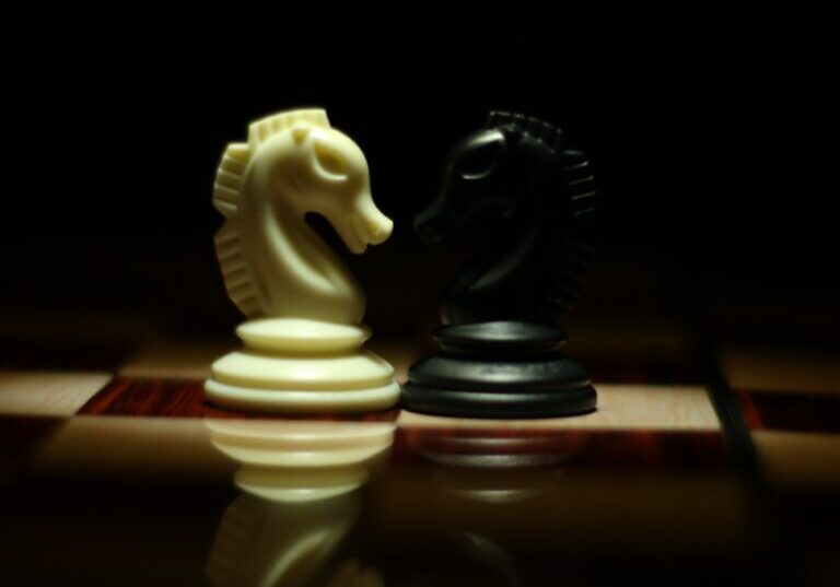 Two chess knights facing each other on a board, one white and one black, highlighted with dramatic lighting in a dark setting, symbolizing a Strategic Meeting Management Program.