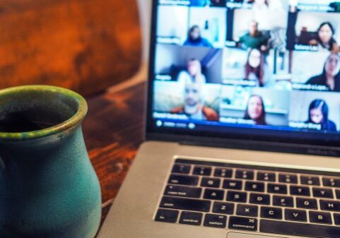 A laptop displaying a digital marketing video conference with multiple participants next to a blue mug on a wooden table.