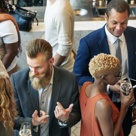 Diverse group of adults conversing and networking at a strategic event procurement, some holding drinks.